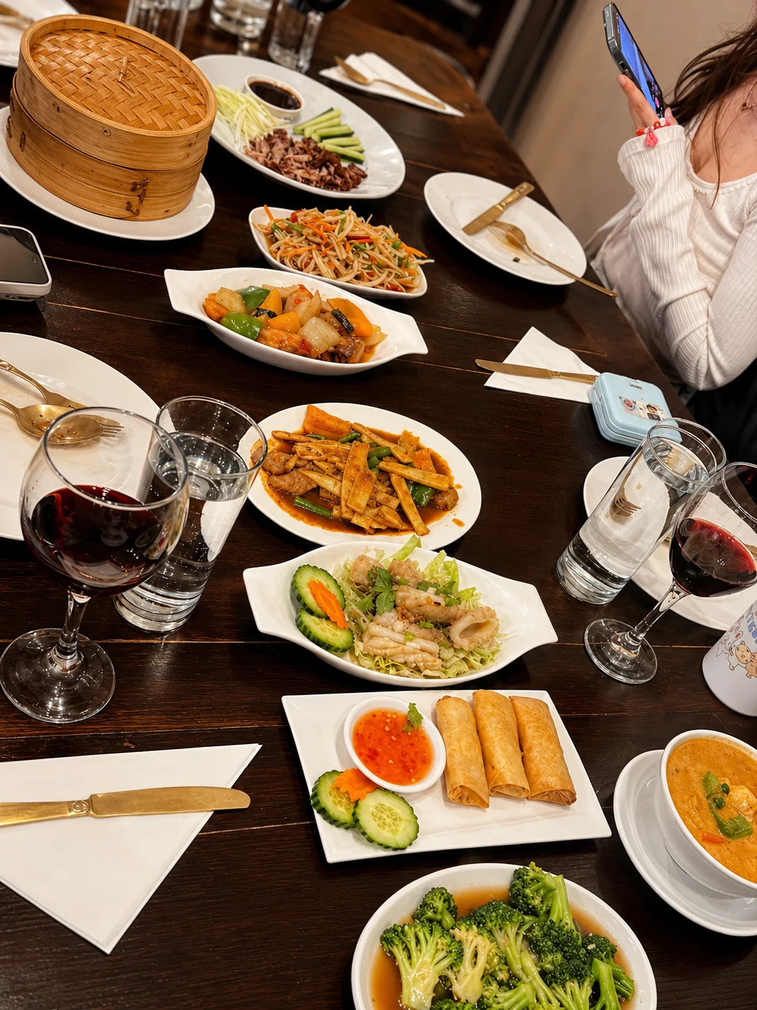 Thai meal spread with spring rolls, broccoli, noodles and wine glasses